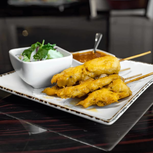 Jasmine Thai Restaurant's chicken satay skewers with peanut sauce and a side salad on a white plate.