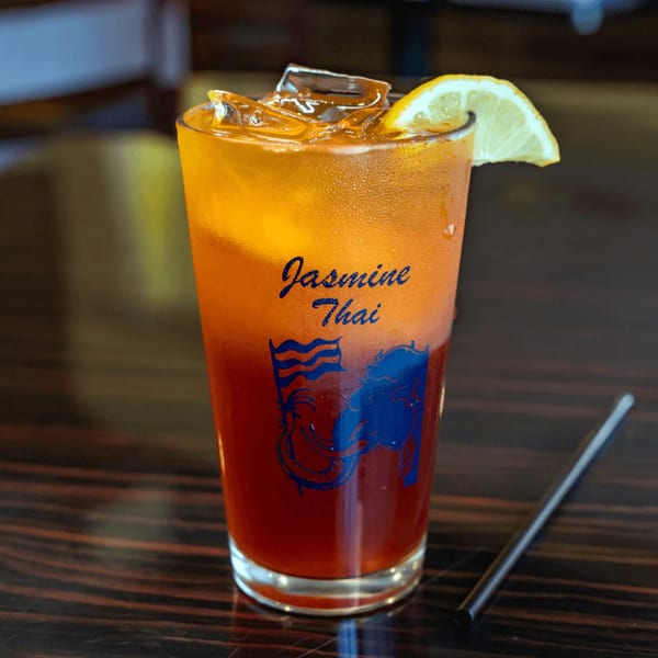 A glass of iced Thai tea with a lemon slice and a straw on a dark wooden table.