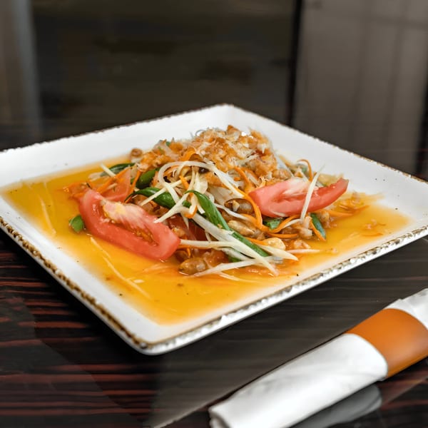 A vibrant Thai papaya salad with tomatoes, green beans, and peanuts in a tangy dressing.