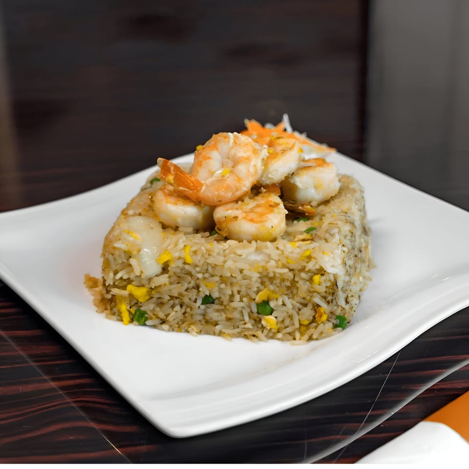 Shrimp fried rice with peas, egg, and carrots on a white rectangular plate.
