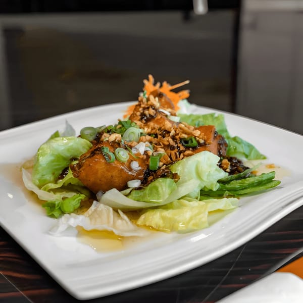 Thai lettuce wraps with chicken, peanuts, scallions, and a dark sauce on a white plate.