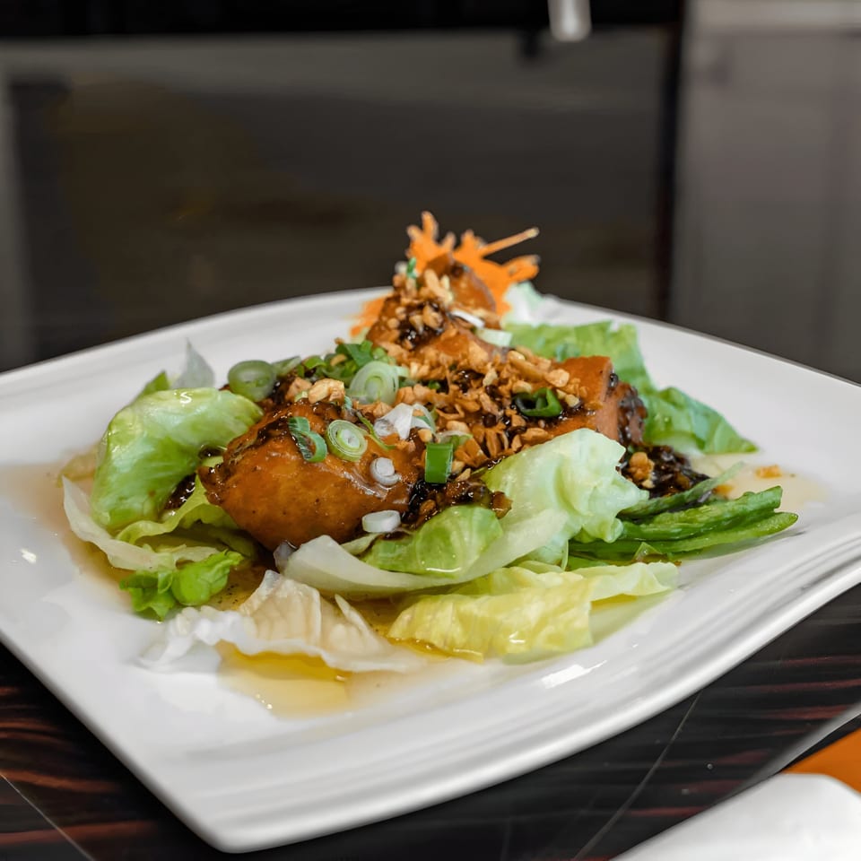 Thai lettuce wraps with chicken, peanuts, scallions, and a dark sauce on a white plate.